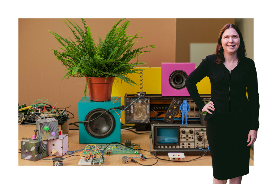 Pictured: Karlene Wightman, Principal Lawyer of Canny Legal. Standing in a black dress with one hand on her hip and smiling. Behind her is an image off a colourful messy desk and colourful speakers.
